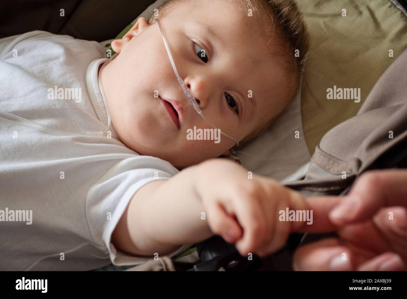 Baby boy with cerebral palsy is getting oxygen. Nasal catheter in a child patient in hospital. Respiratory support. Child on oxygen therapy holding mo Stock Photo