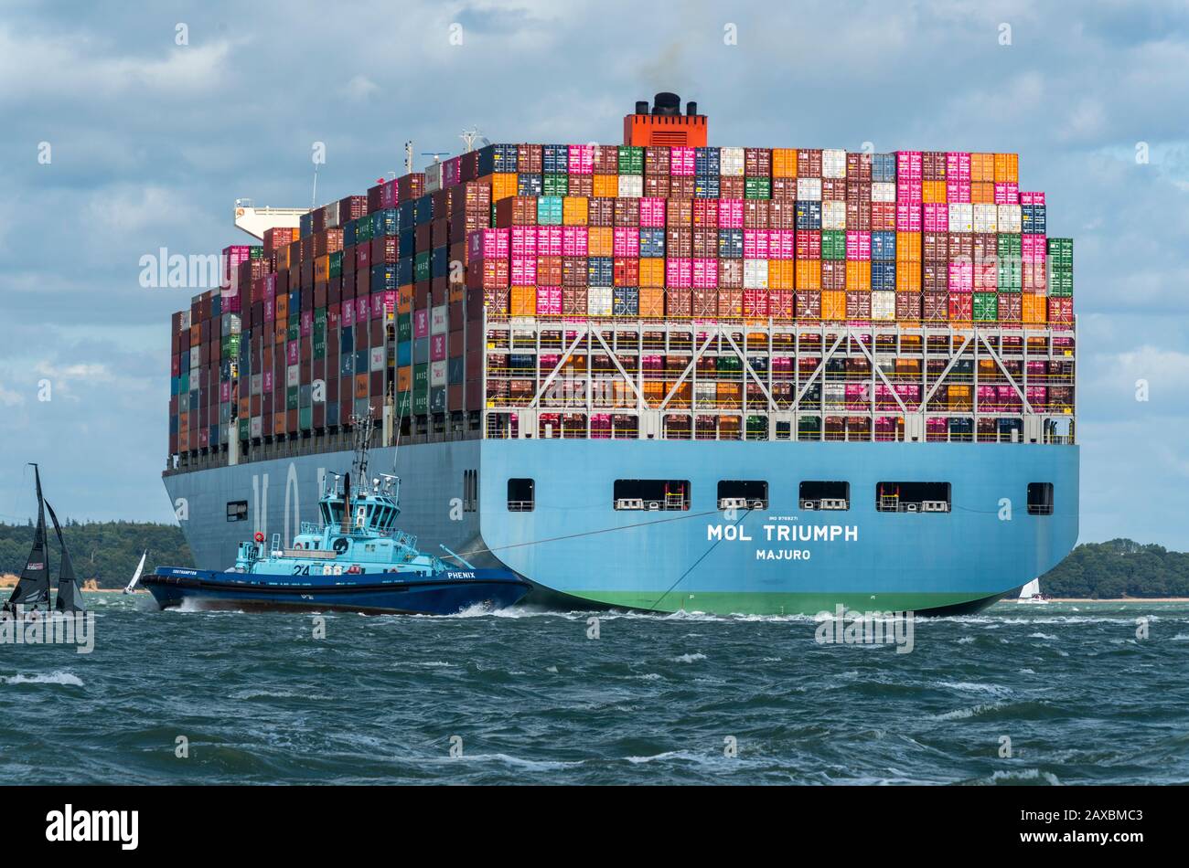 a large container cargo ship entering the port of southampton docks with a tug helping to steer the large massive seagoing vessel in the solent. Stock Photo
