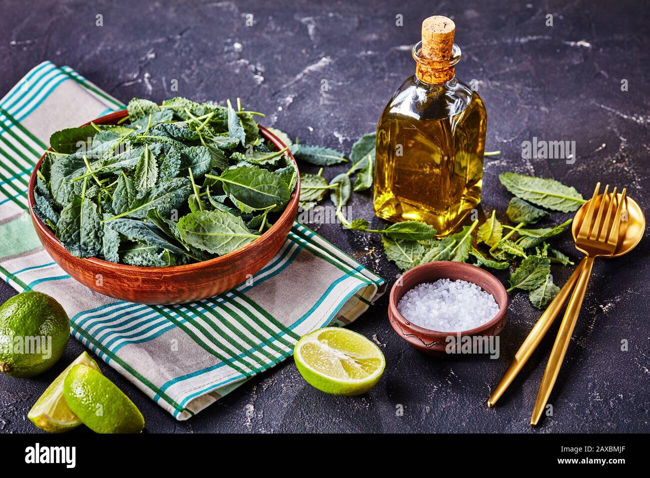 Healthy eating lifestyle: fresh kale leaves on a bowl, served with sea salt and olive oil, salad utensils and lime on dark concrete background, horizo Stock Photo