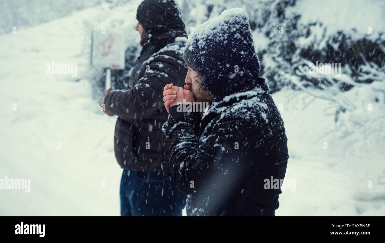 The cold men is waiting for the bus while it snows on a winter day. Transportation concept in winter. Stock Photo