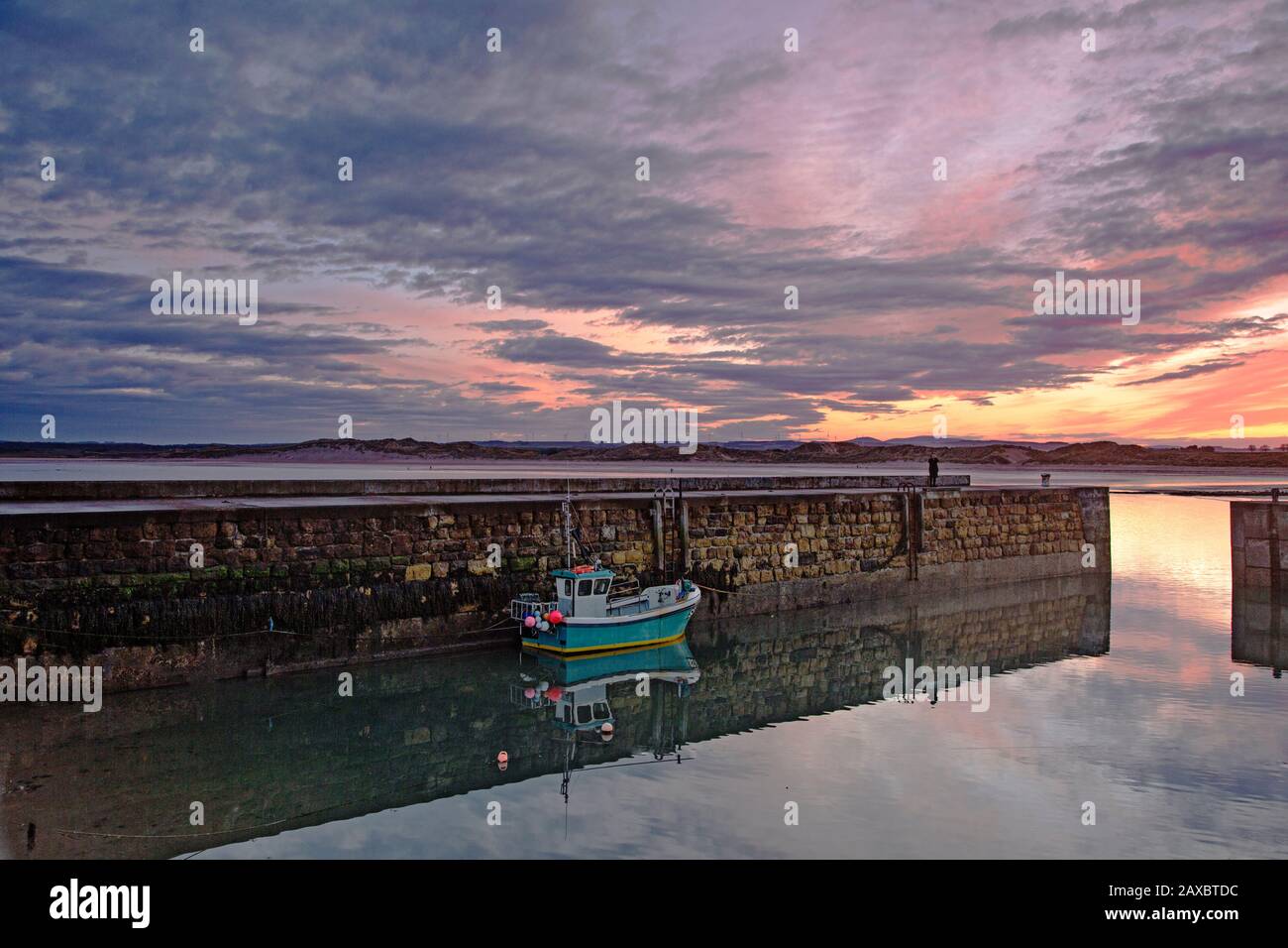 Fishing boot moored along jetty wall under dramatic sunrise sky Stock Photo