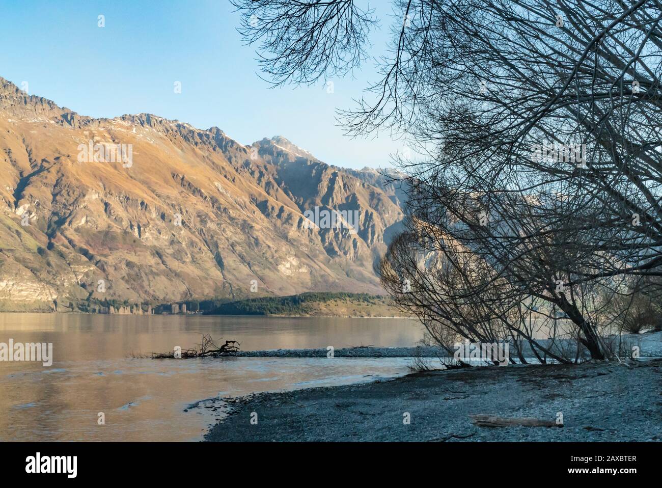 Sunlight bathes the opposite bank of Lake Wakatipu from Twelve Mile Delta near Queenstown - used as Ithilien in the Lord of the Rings. Stock Photo