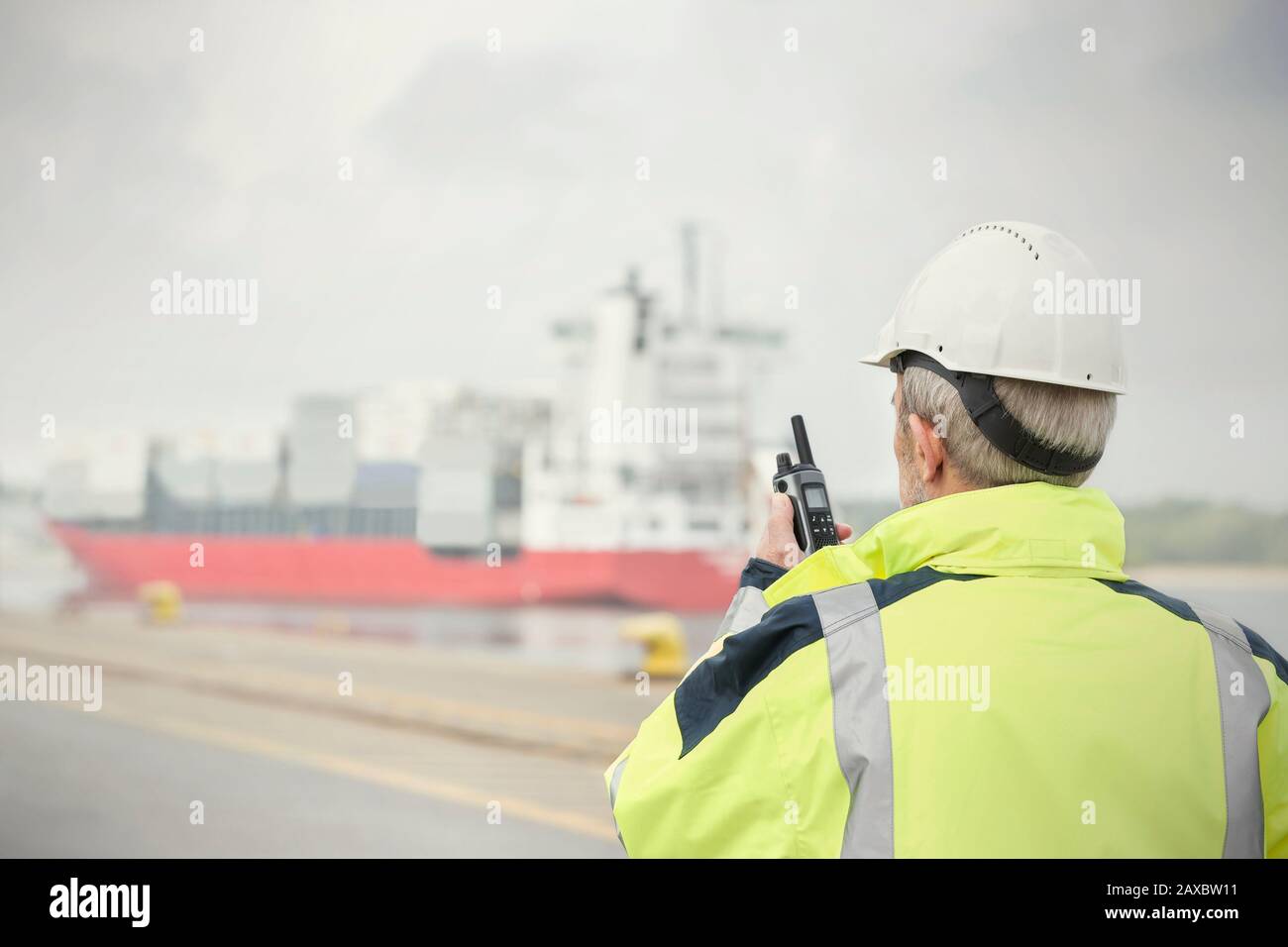 Dock manager with walkie-talkie watching container ship at commercial dock Stock Photo