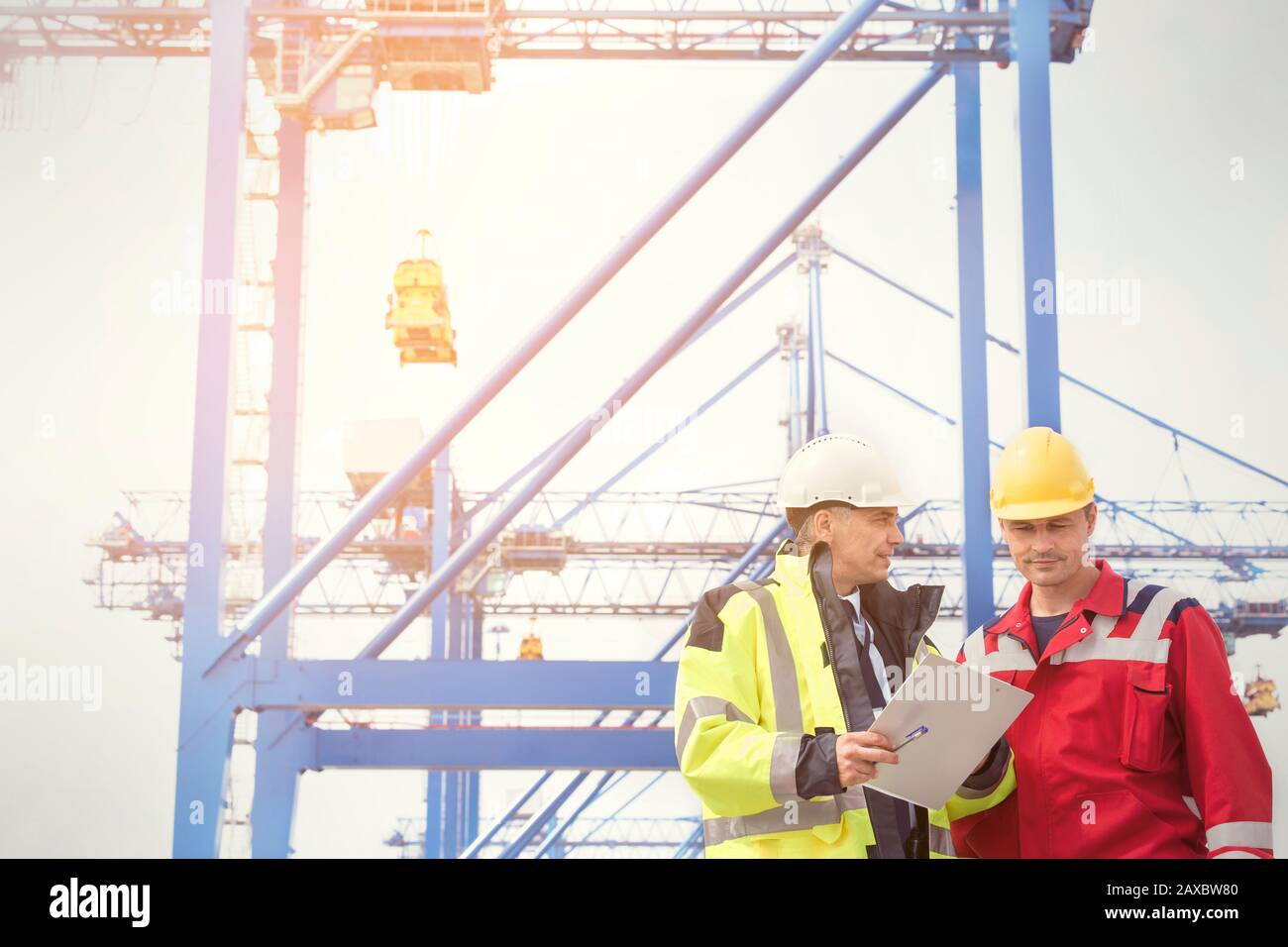 Dock worker and manager with clipboard talking below crane at shipyard Stock Photo