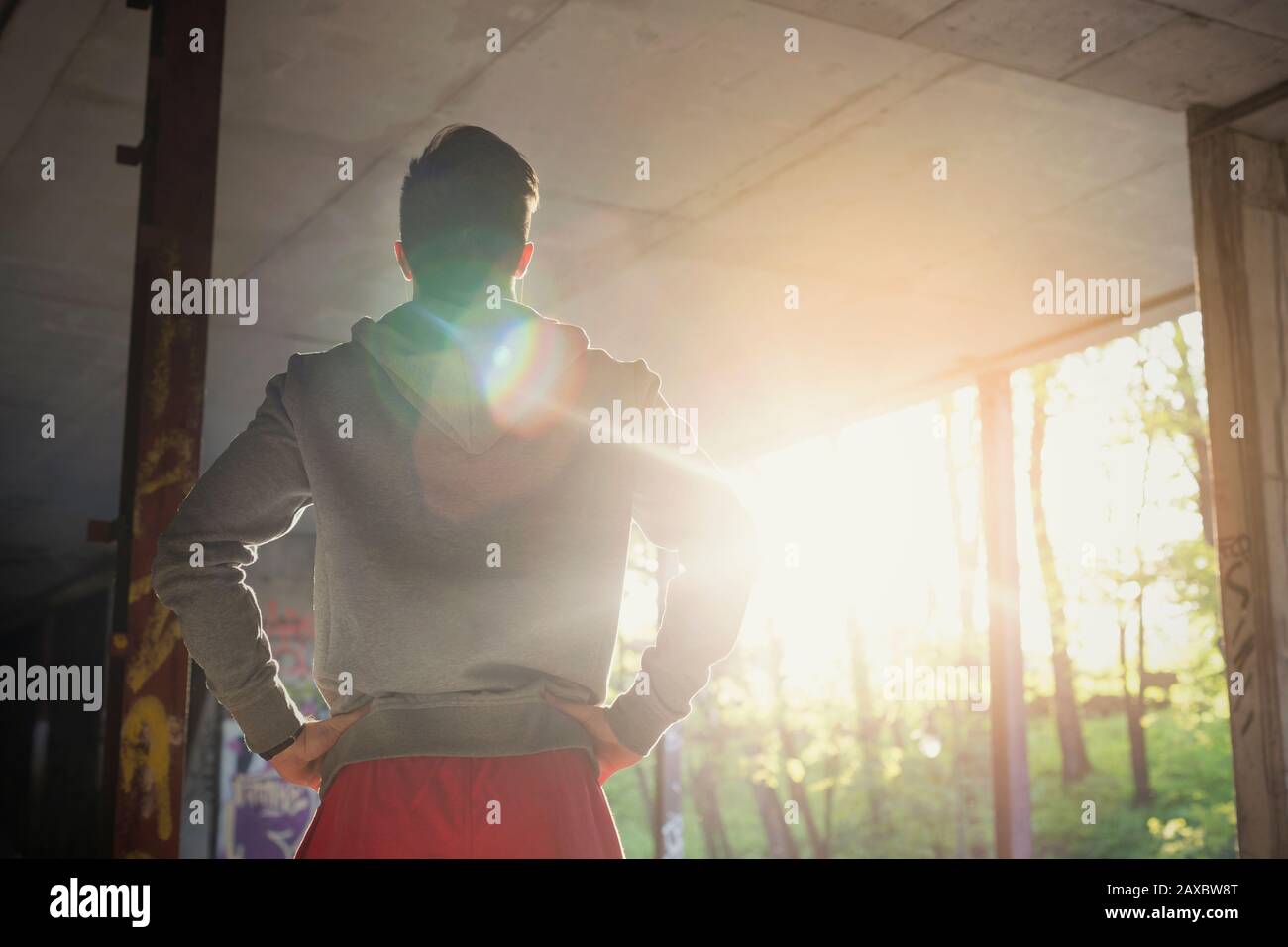 Young male runner resting, standing with hands on hips in sunny abandoned building Stock Photo