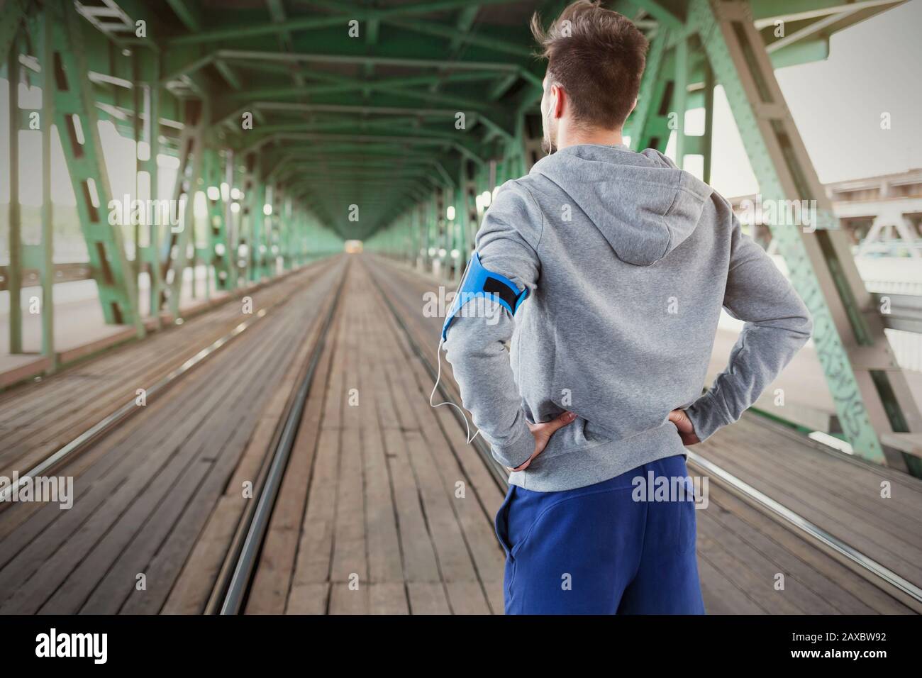 Young male runner standing on train tracks with hands on hips Stock Photo