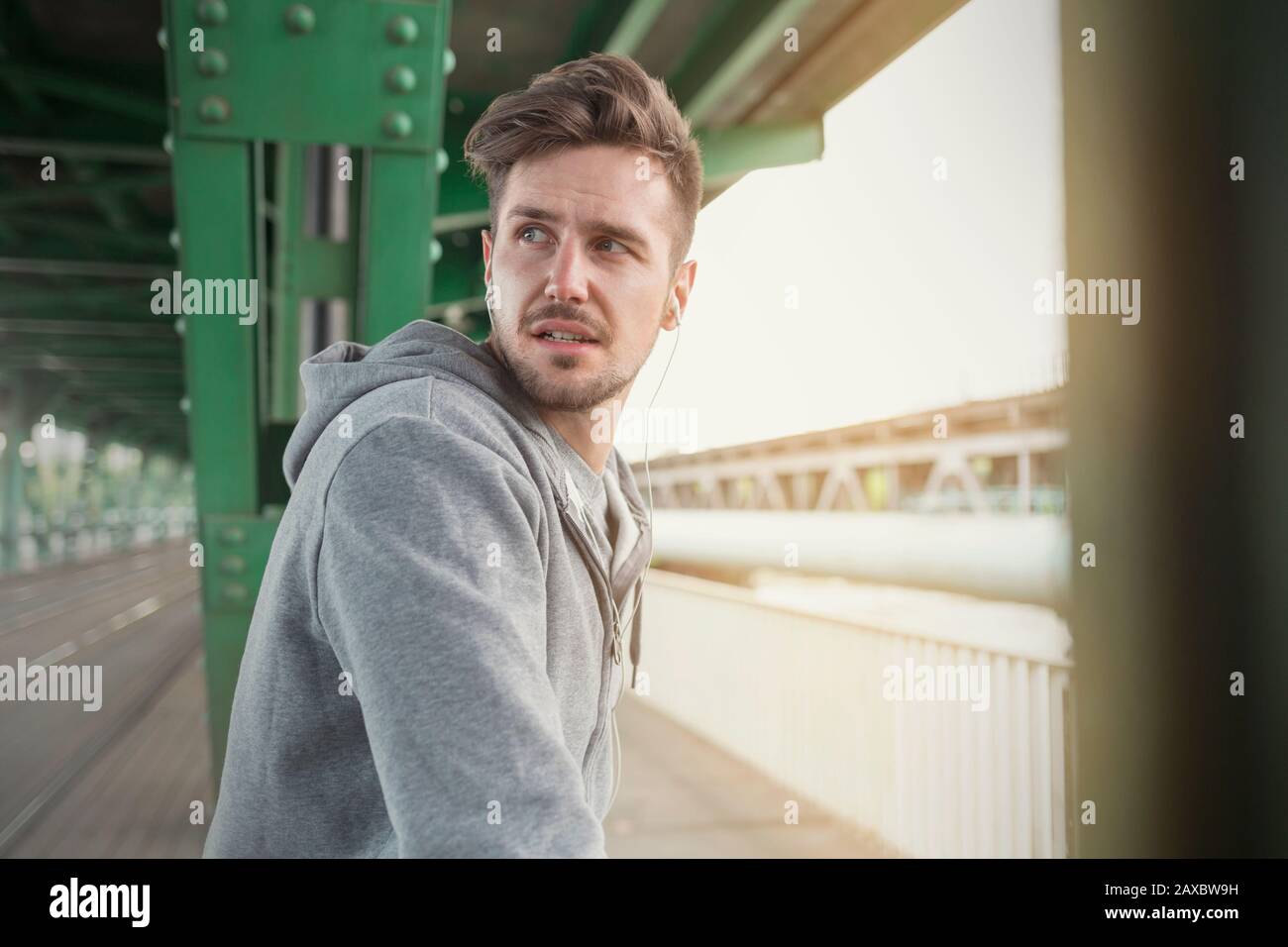 Young male runner with headphones looking over shoulder on train station platform Stock Photo