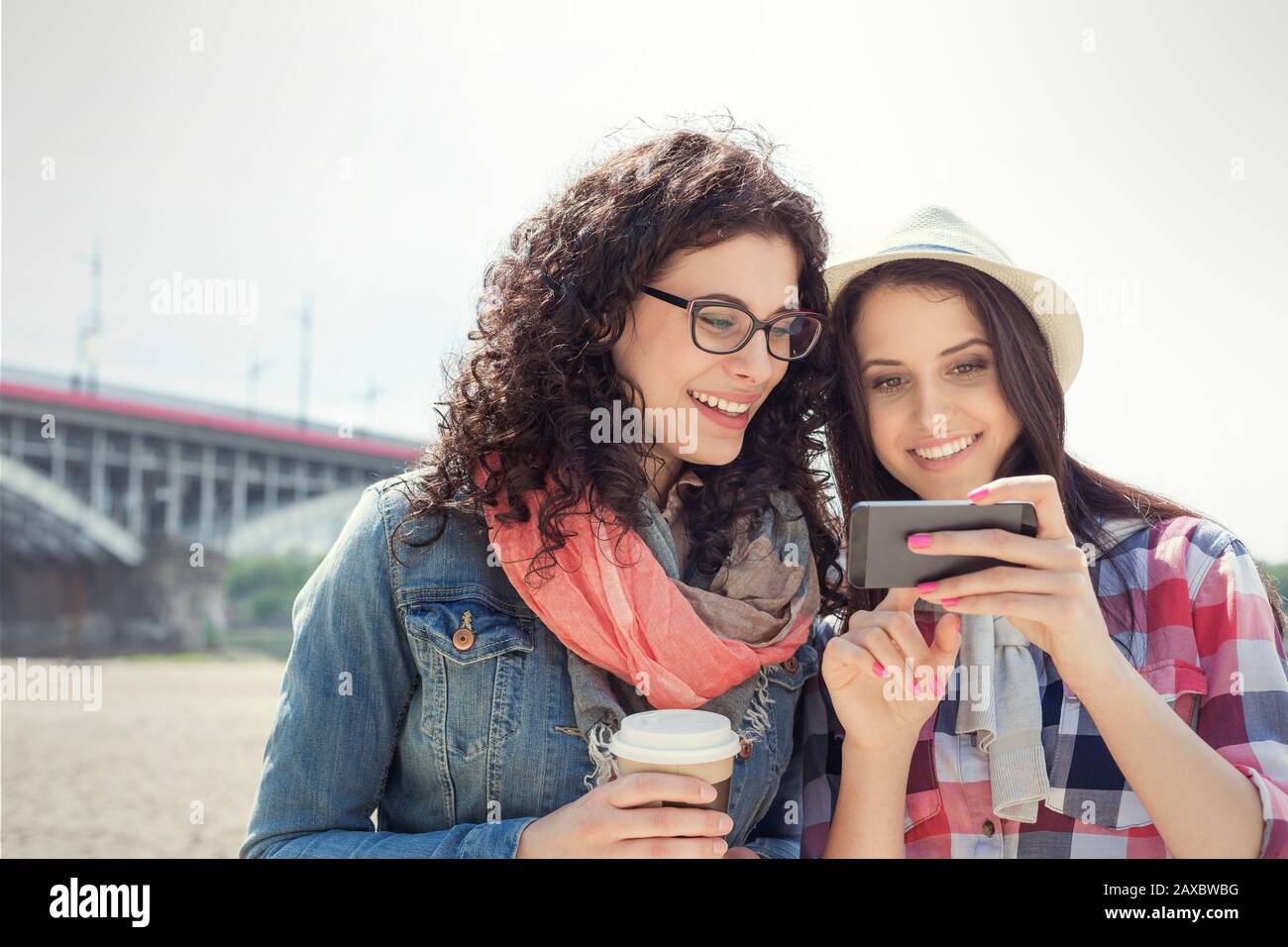 Young women friends using smart phone and drinking coffee outdoors Stock Photo