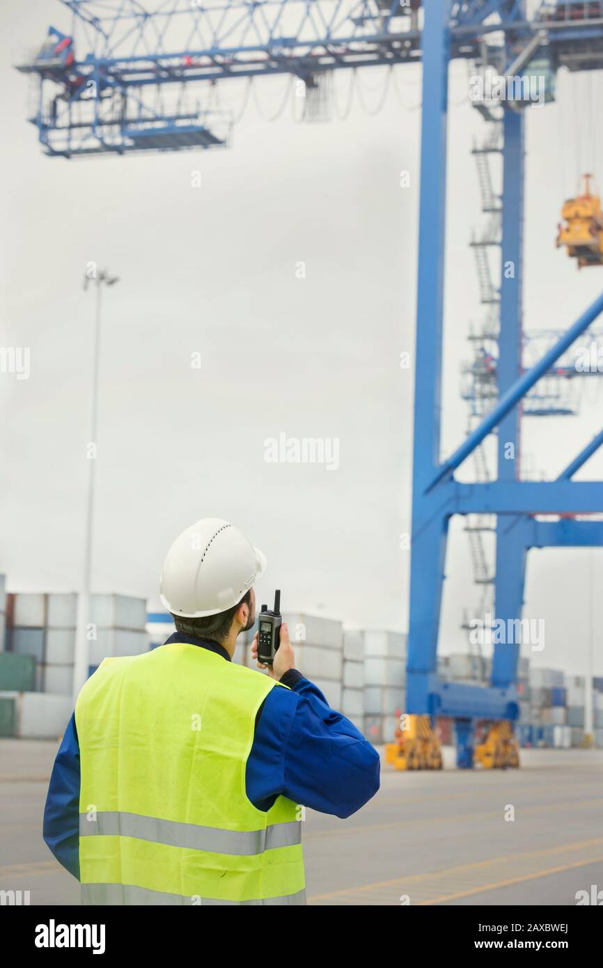 Dock worker with walkie-talkie watching crane at shipyard Stock Photo
