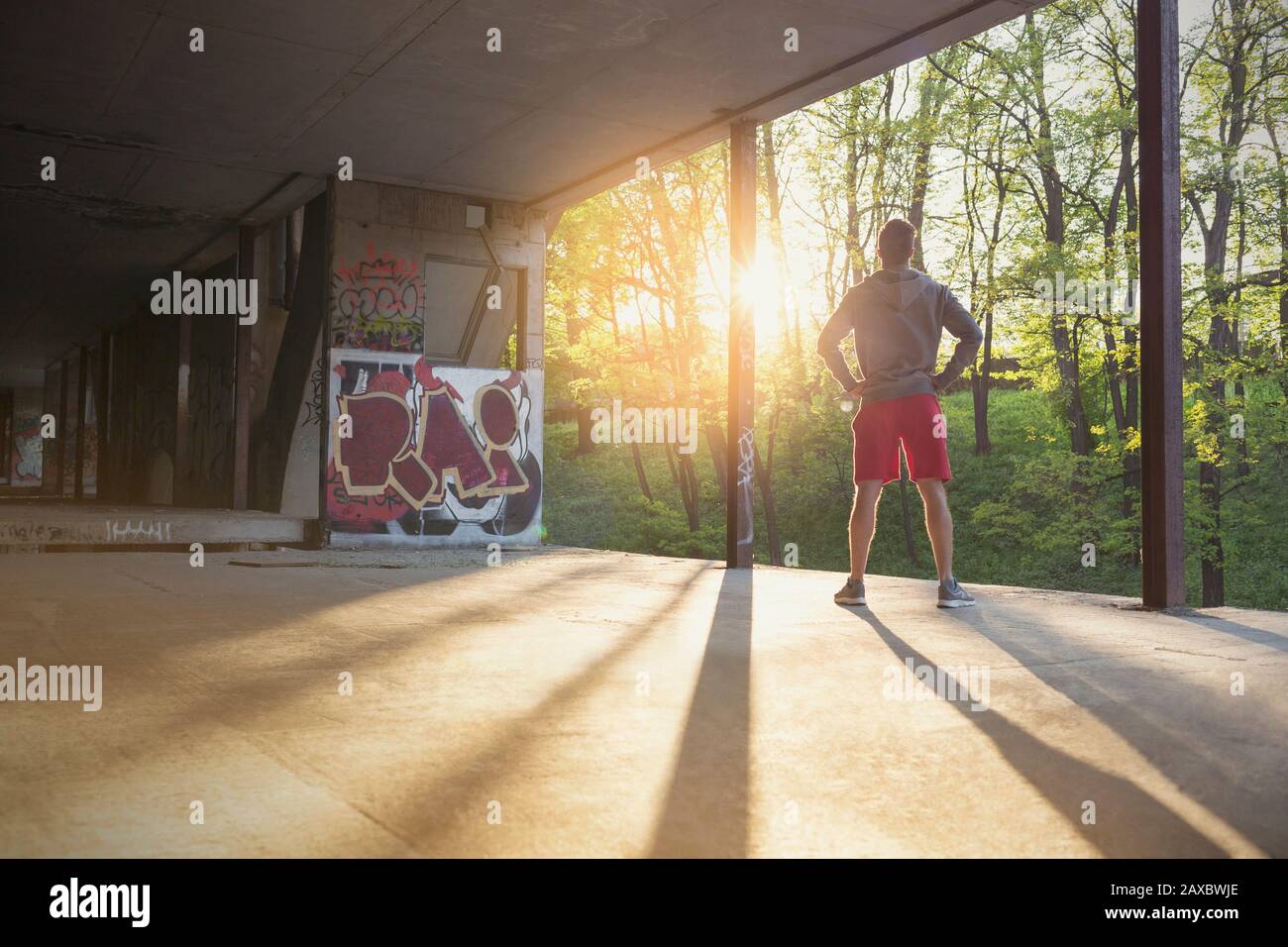 Young male runner resting with hands on hips in sunny abandoned building Stock Photo