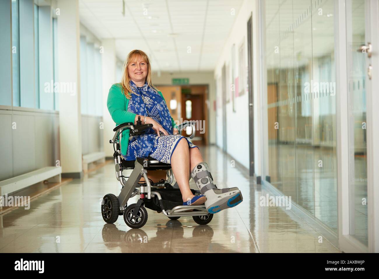 Portrait smiling woman wearing medical boot in wheelchair in corridor