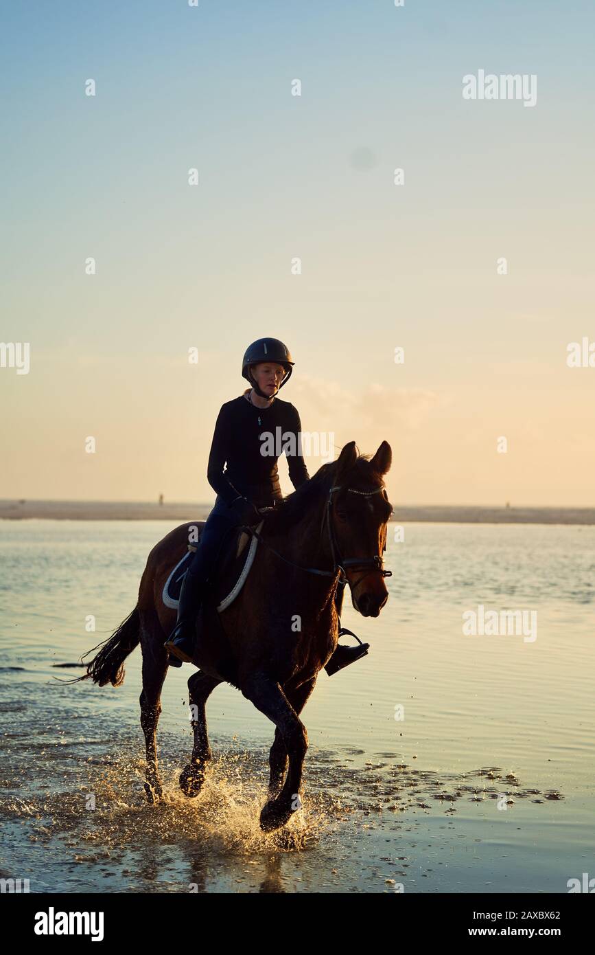 Young woman horseback riding in ocean surf Stock Photo