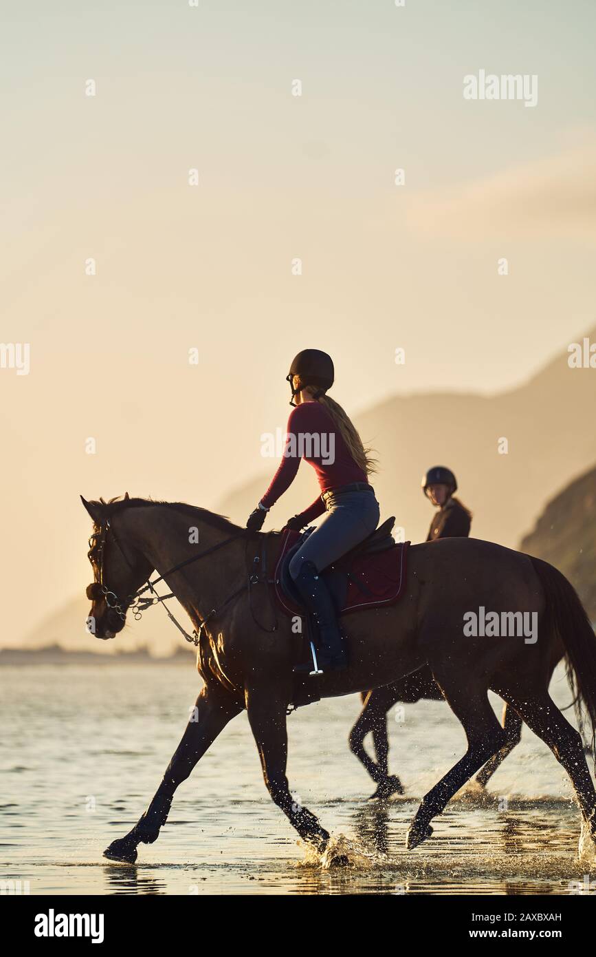 Young woman horseback riding on ocean beach at sunset Stock Photo