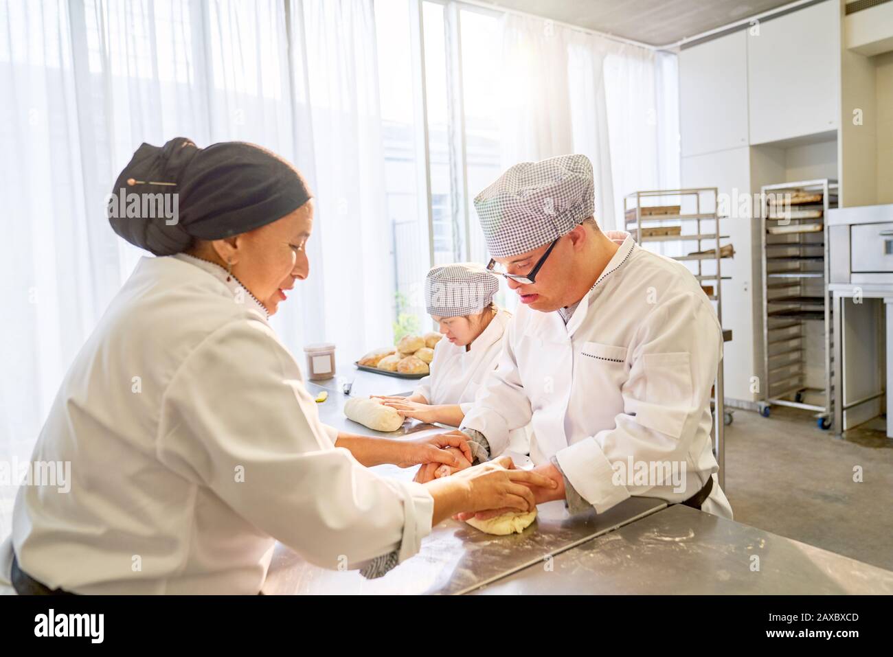 Chef helping Down Syndrome students roll dough in kitchen Stock Photo