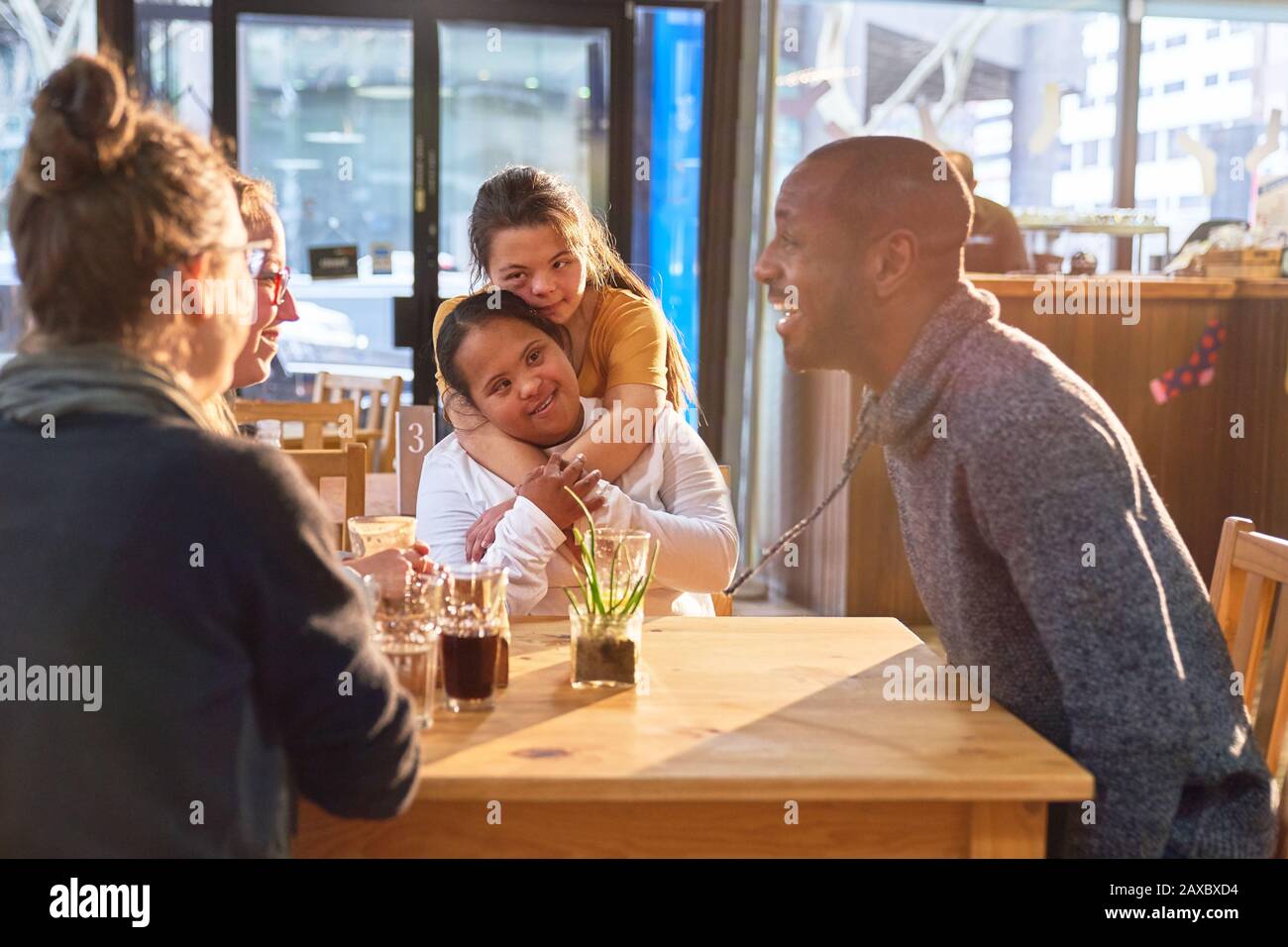 Affectionate young women with Down Syndrome in cafe with friends Stock Photo