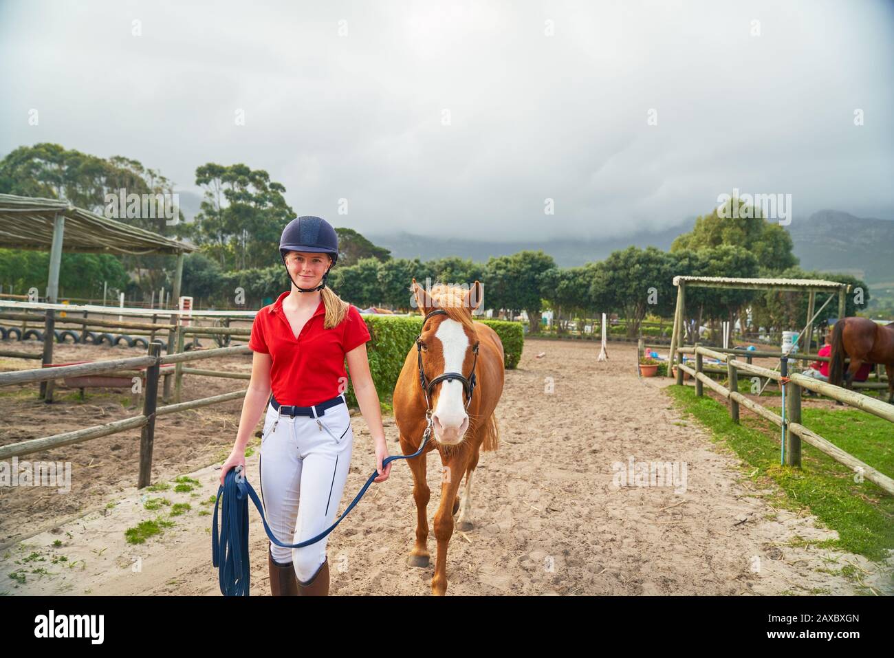 Portrait confident teenage girl leading horse along rural paddocks Stock Photo