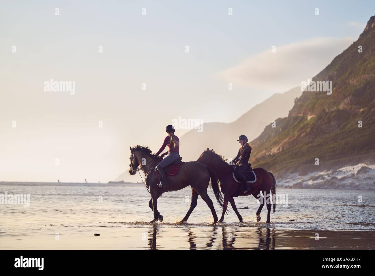 Young women horseback riding on tranquil ocean beach Stock Photo