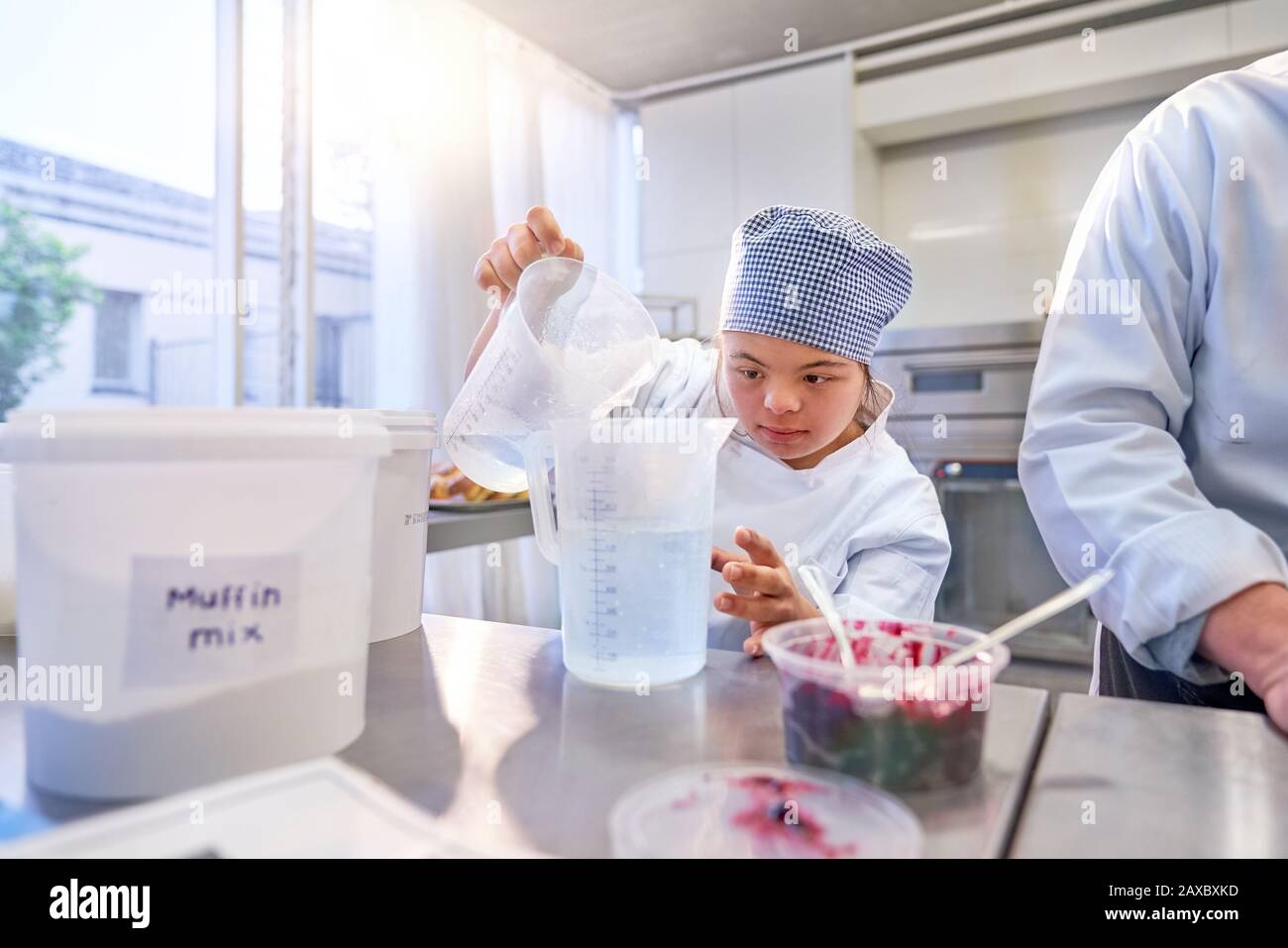 Focused young female student with Down Syndrome baking in kitchen Stock Photo