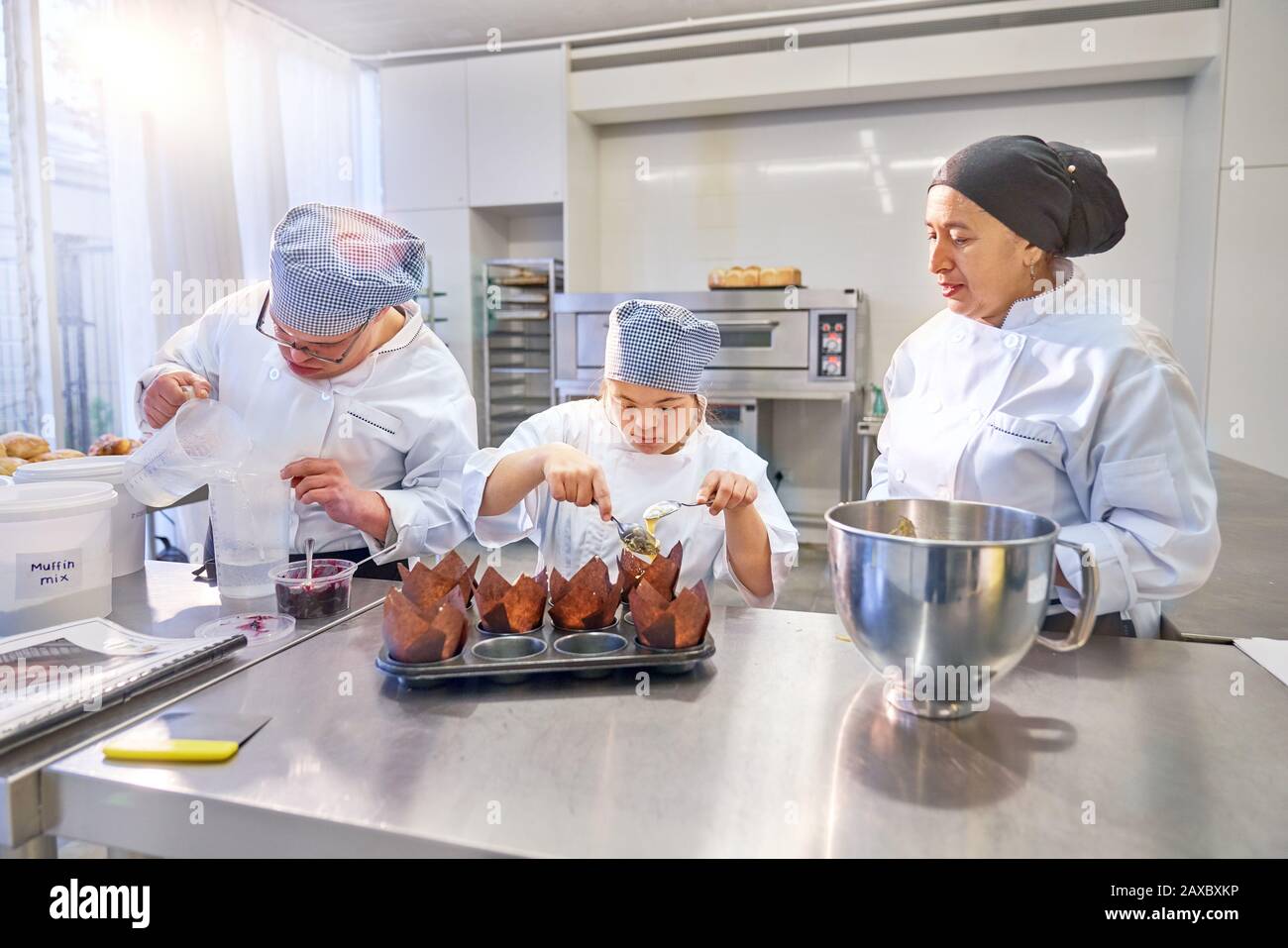Chef helping students with Down Syndrome baking muffins in kitchen Stock Photo