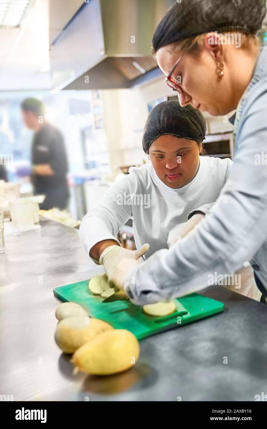 Chef and young woman with Down Syndrome cutting potatoes in kitchen Stock Photo