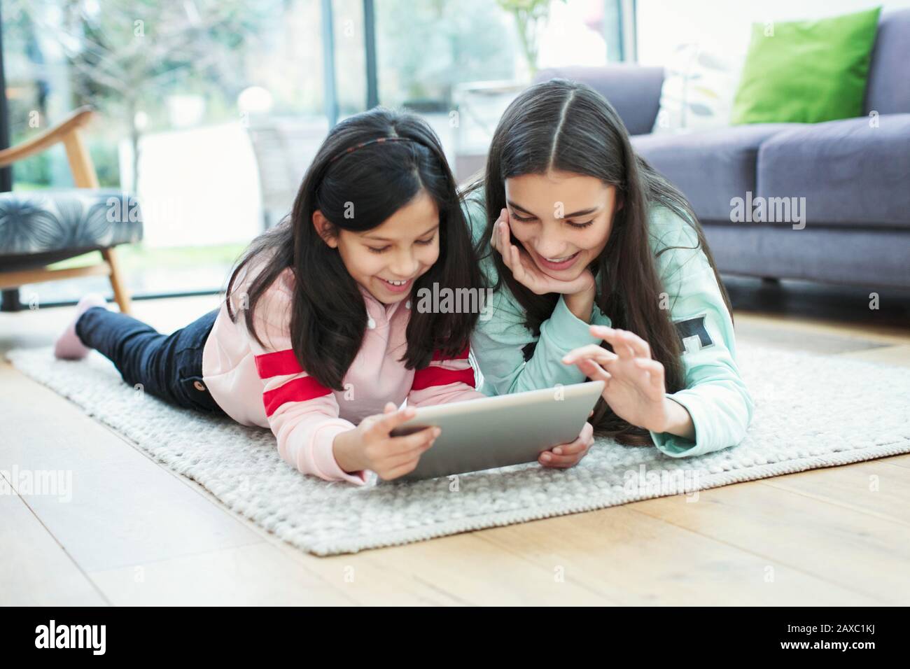 Smiling sisters using digital tablet on living room floor Stock Photo