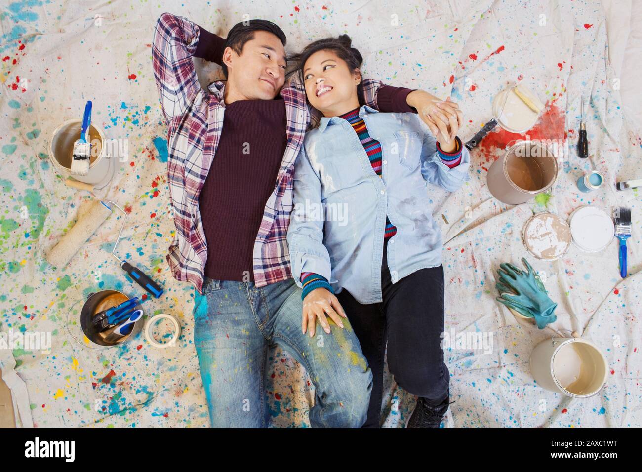 Happy couple relaxing, taking a break from painting, laying on dropcloth among paint cans Stock Photo