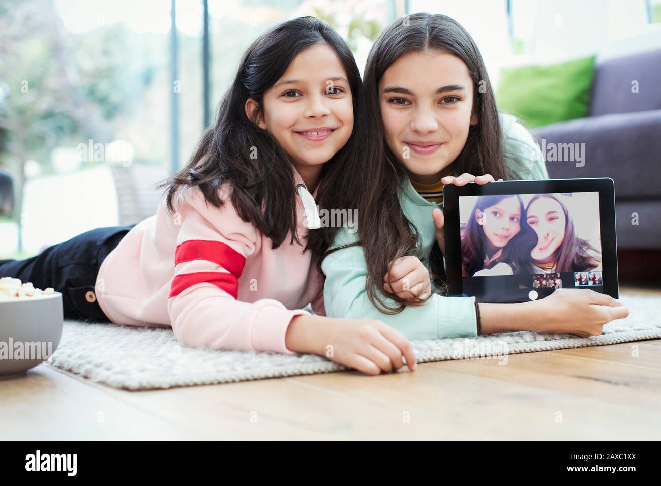 Portrait smiling sisters using digital tablet camera on living room ...