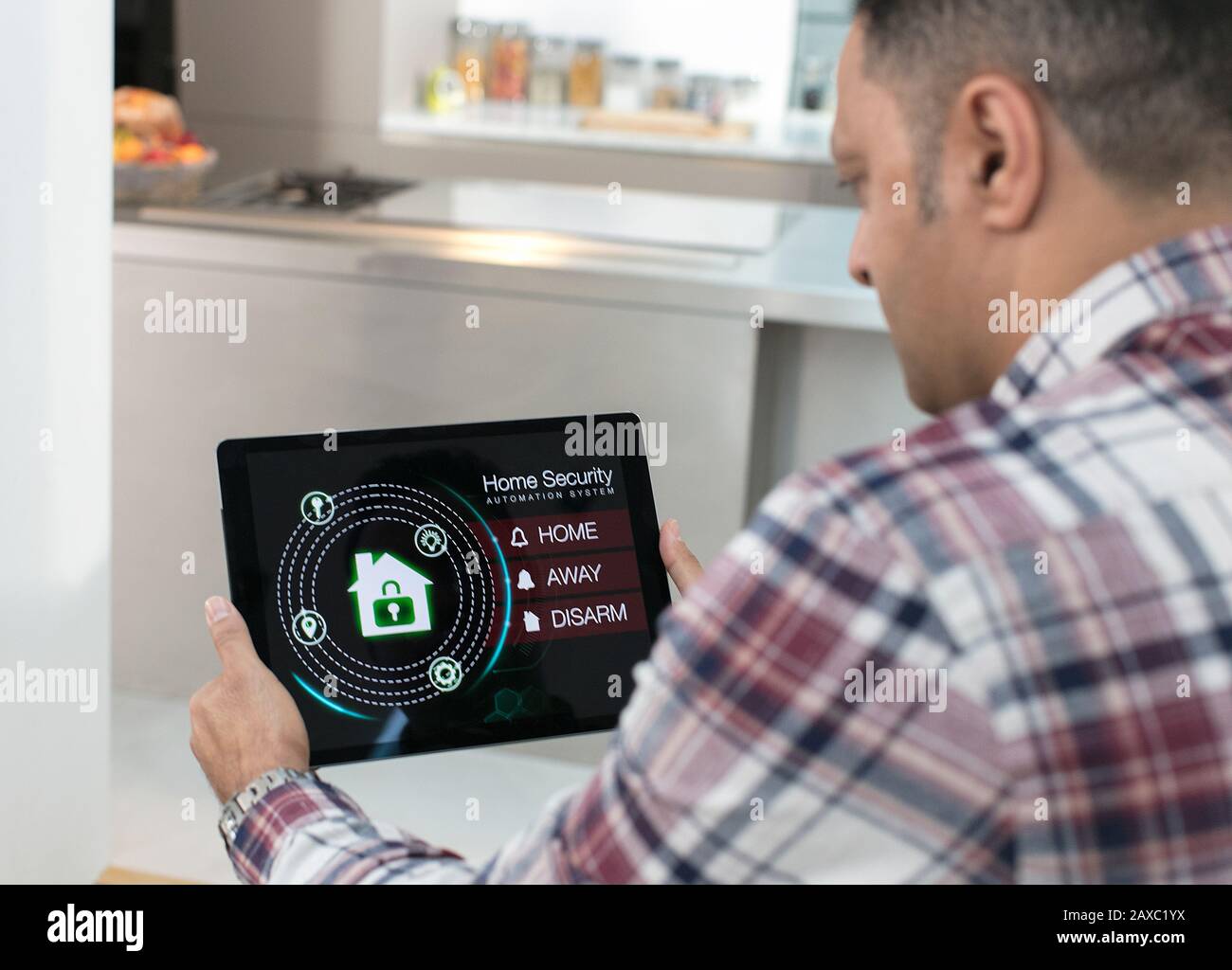 Man setting smart home security alarm from digital tablet in kitchen Stock Photo