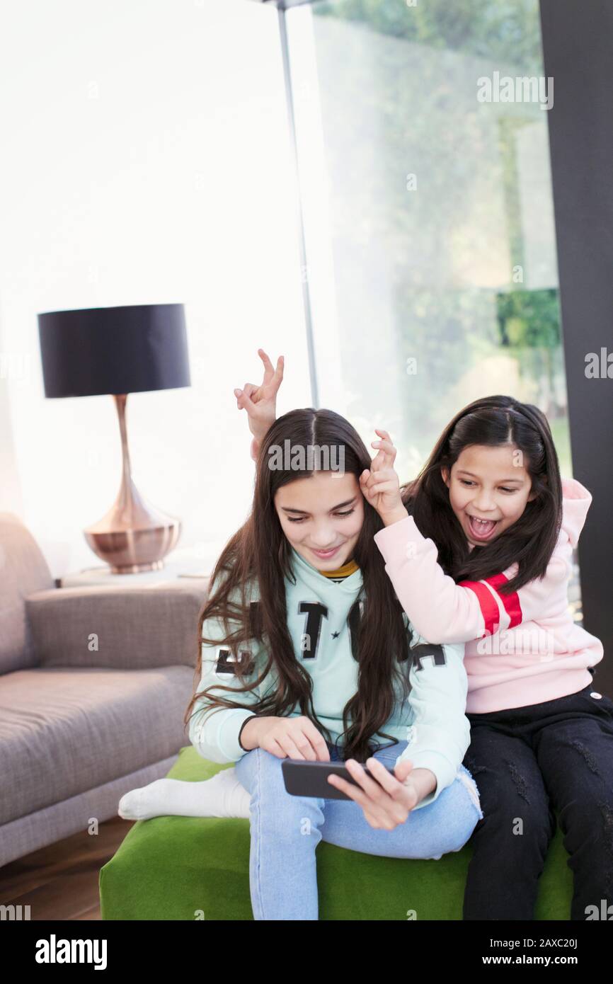 Playful sisters taking selfie with smart phone in living room Stock Photo