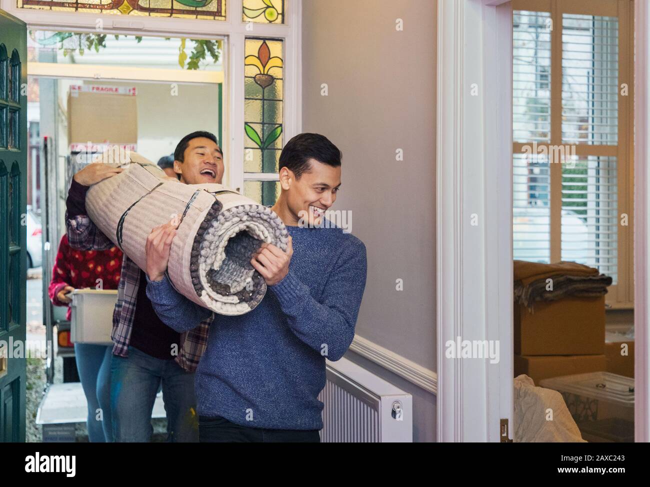 Men moving house, carrying rug in corridor Stock Photo