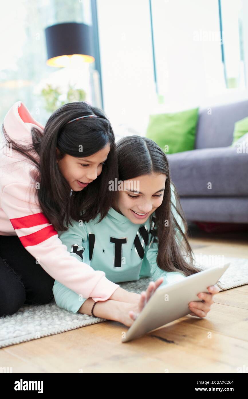 Sisters using digital tablet on living room floor Stock Photo