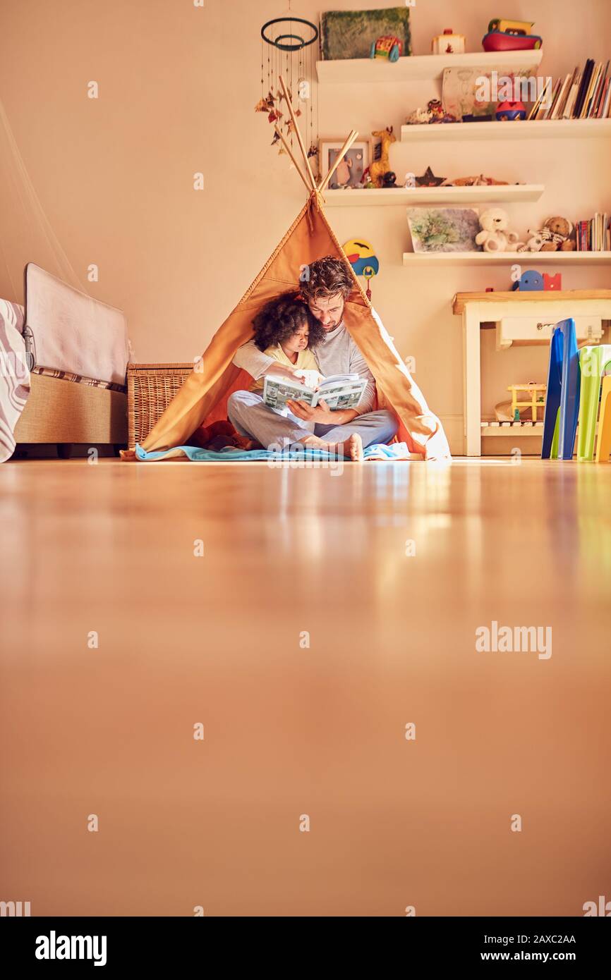 Father and daughter reading book in teepee Stock Photo