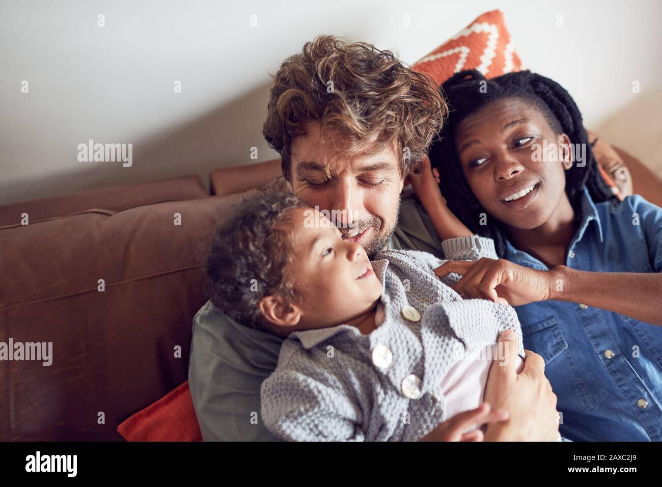 Affectionate young family cuddling on sofa Stock Photo