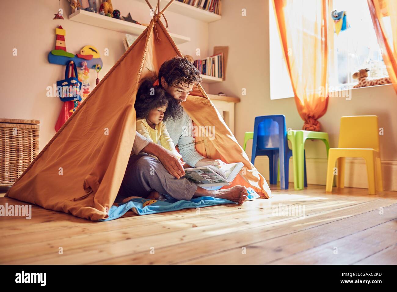 Father and toddler daughter reading book in teepee Stock Photo