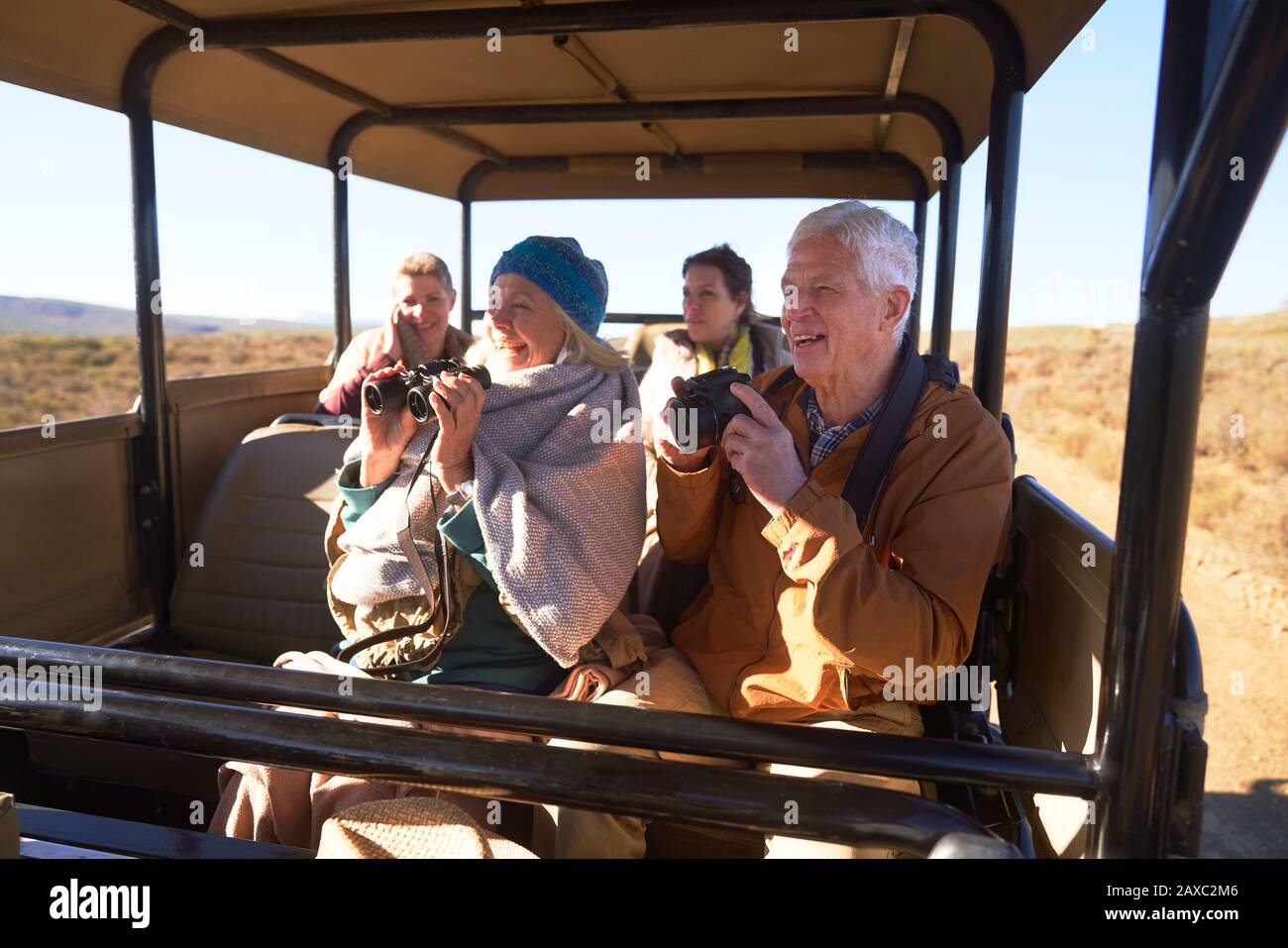 Happy seniors with binoculars and camera on safari in off-road vehicle Stock Photo