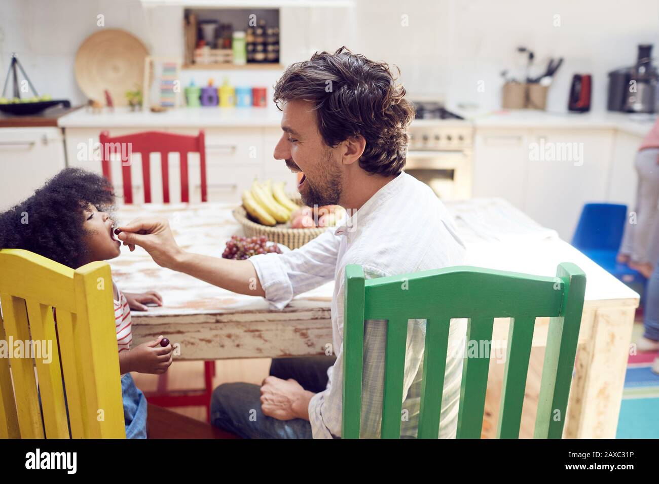 Father feeding daughter grapes at kitchen table Stock Photo