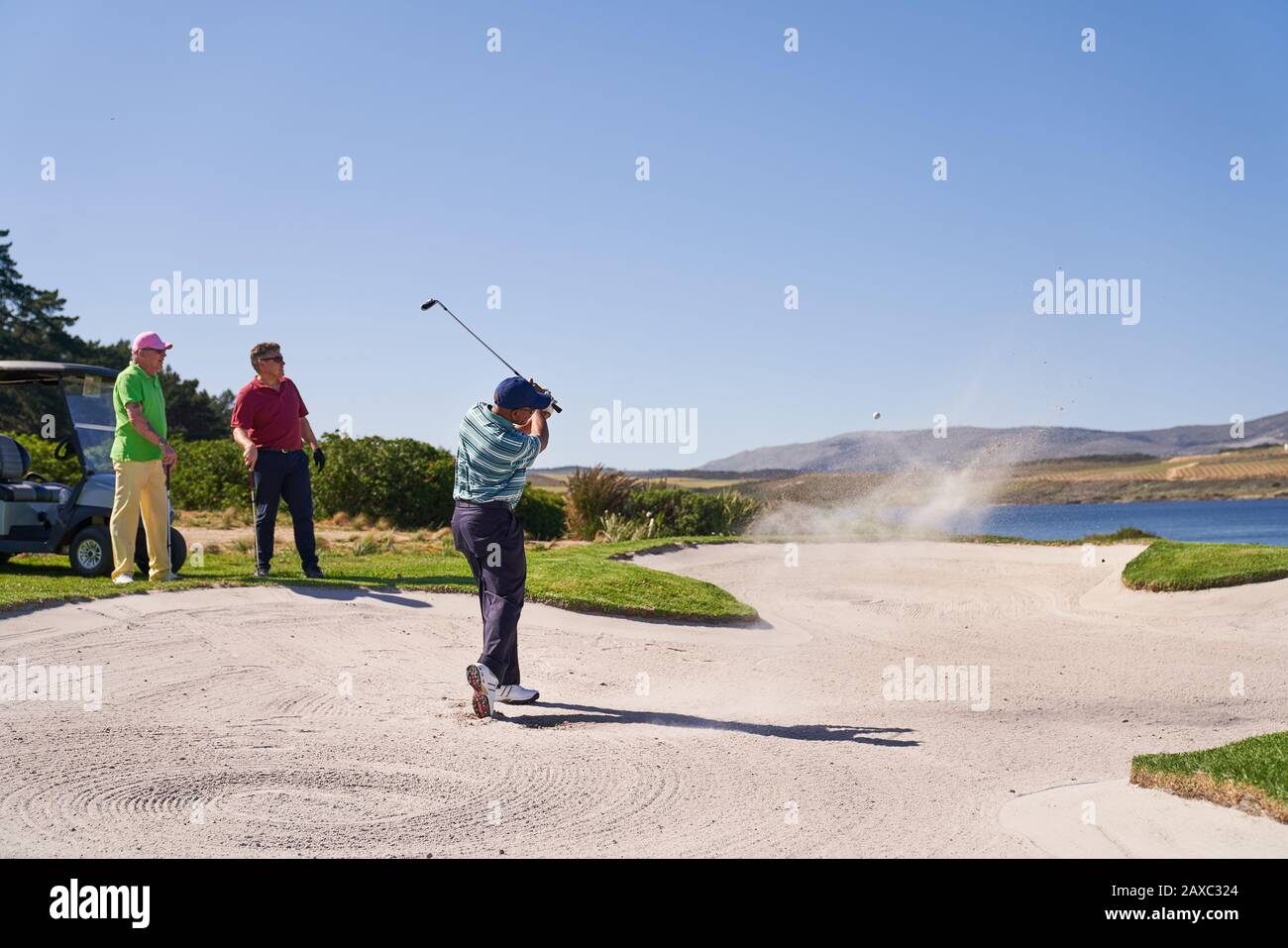 Man taking shot out of bunker on sunny golf course Stock Photo