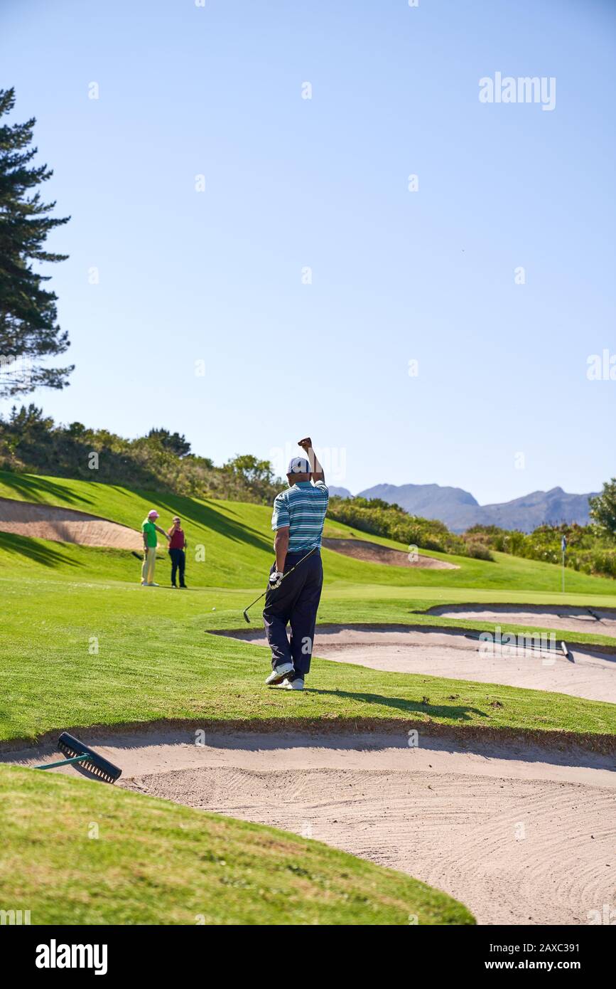 Happy man golfing cheering on sunny golf course Stock Photo