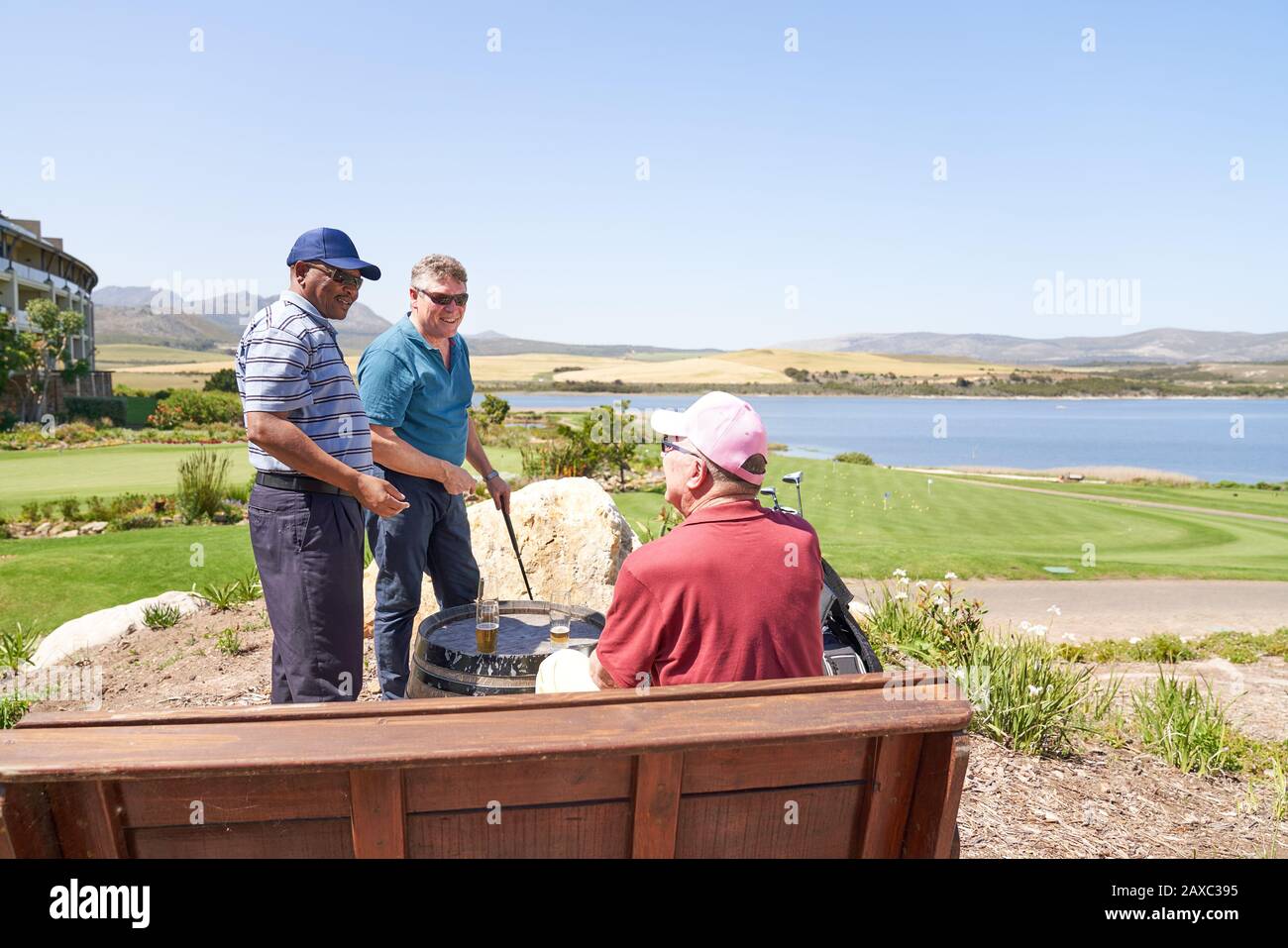 Male golfer friends talking drinking beer on sunny golf course patio Stock Photo