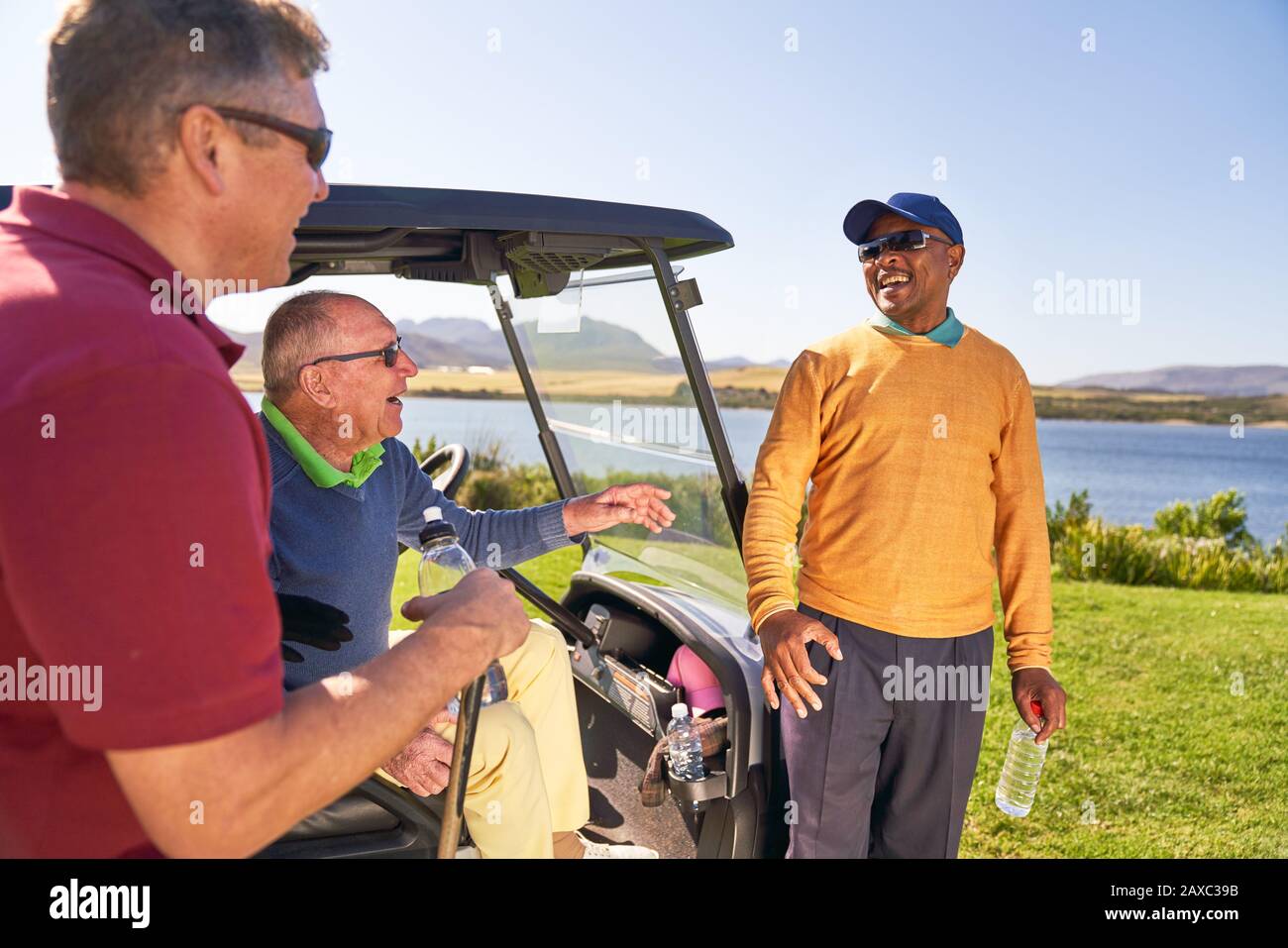Male golfer friends talking and laughing at golf cart Stock Photo