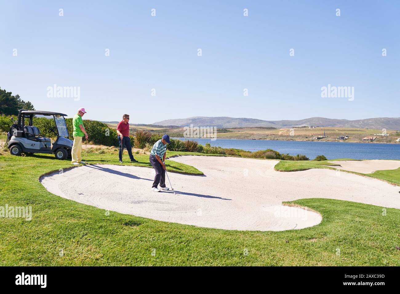 Man taking shot out of bunker on sunny golf course Stock Photo