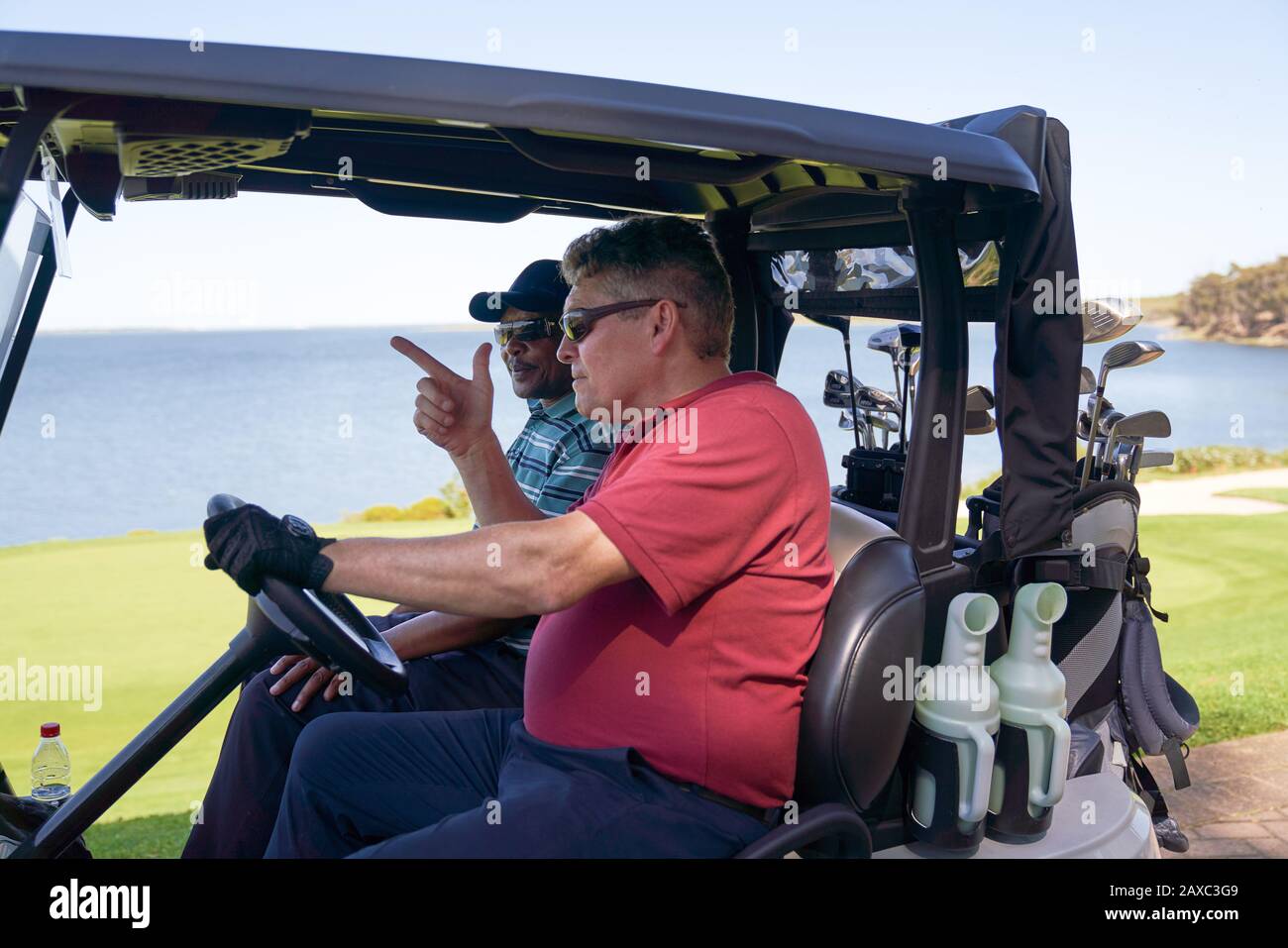 Male golfers driving golf cart on lakeside golf course Stock Photo