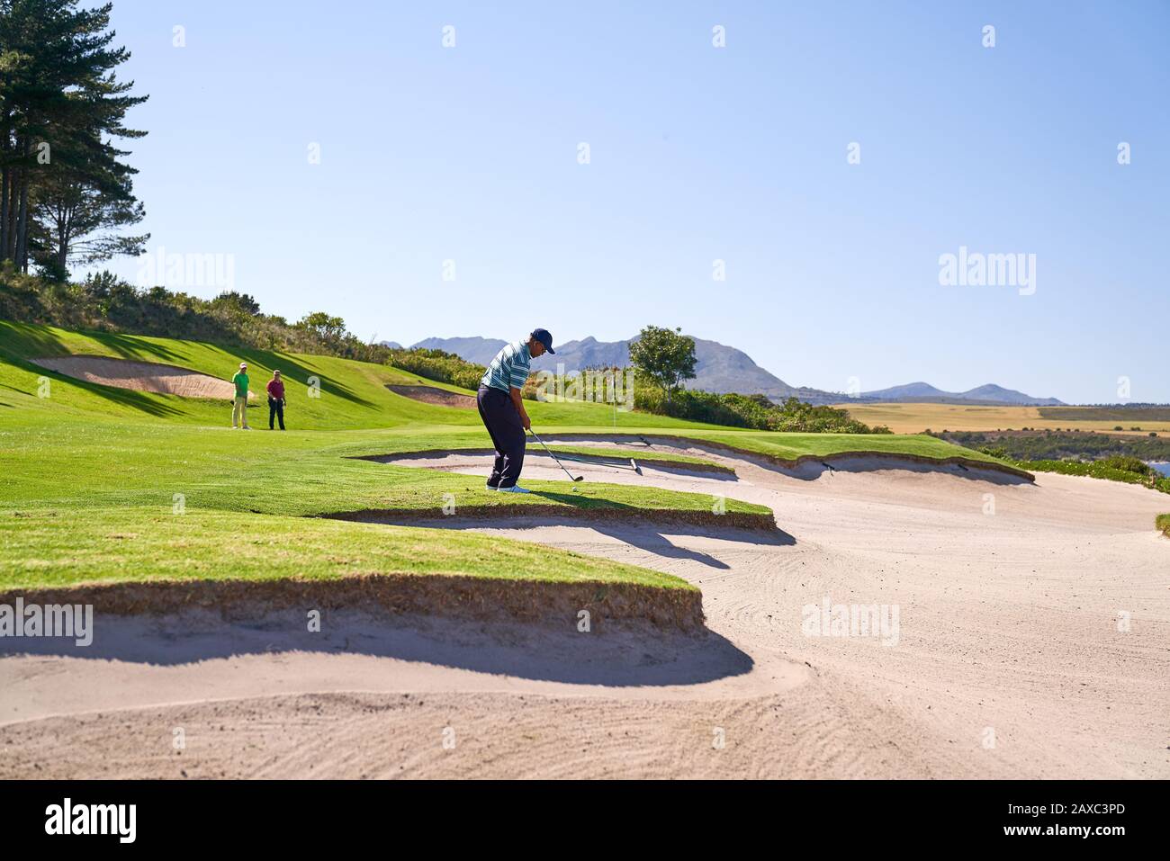 Male golfer taking a shot above sunny sand trap Stock Photo