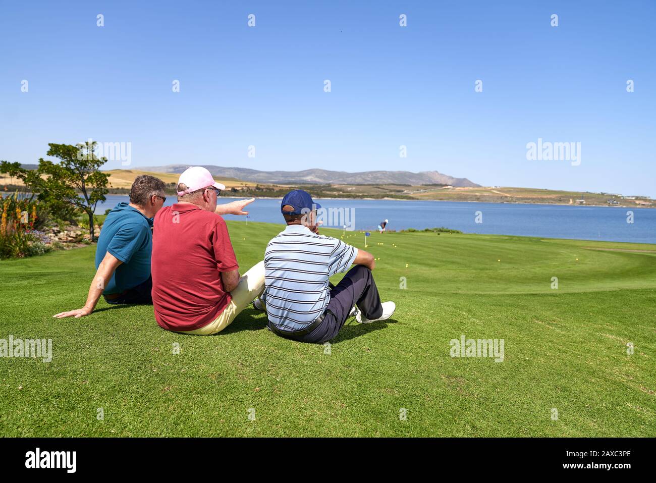 Male golfers relaxing looking at lake view from sunny golf course Stock Photo