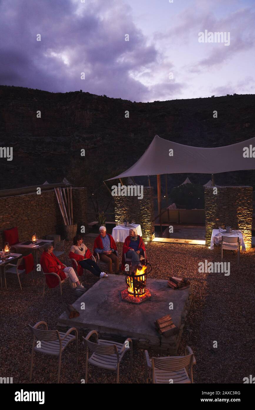 Senior friends relaxing at fire pit on hotel patio Stock Photo