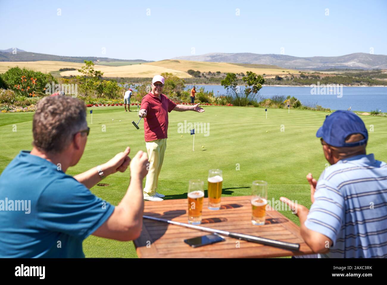 Happy male golfers drinking beer and practicing putting at golf course Stock Photo