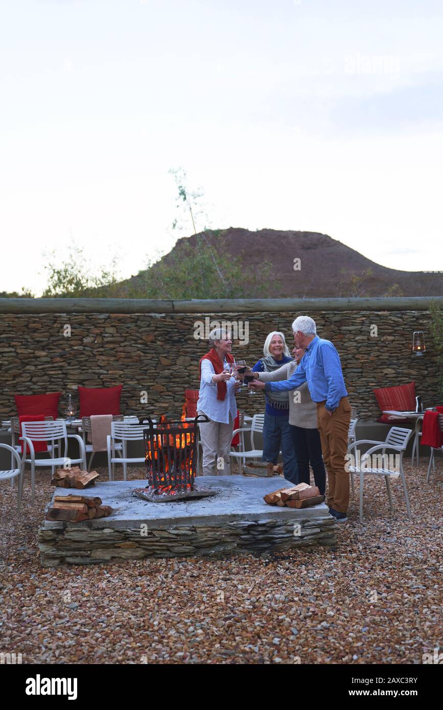 Happy senior friends drinking wine at hotel patio fire pit Stock Photo