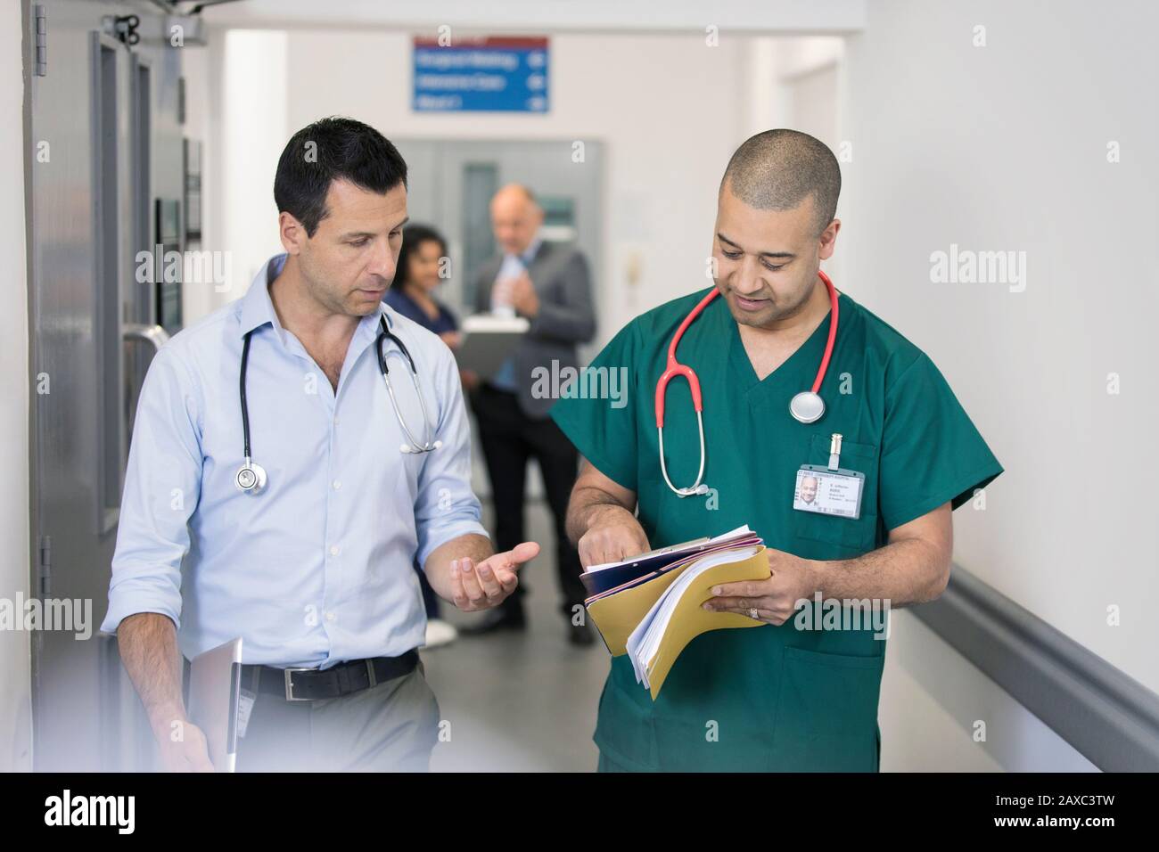 Male doctor and surgeon discussing medical chart, making rounds in hospital corridor Stock Photo