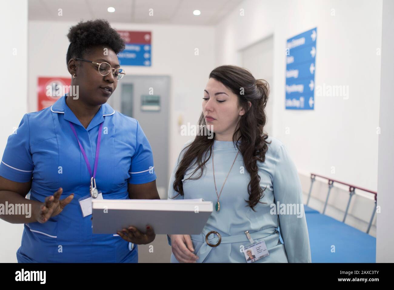 Female doctor and nurse making rounds, discussing medical chart in hospital corridor Stock Photo