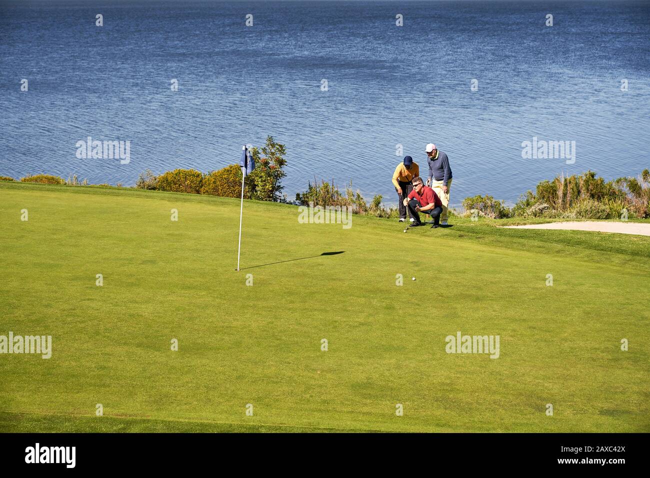 Male golfers planning putt shot at sunny lakeside golf course Stock Photo